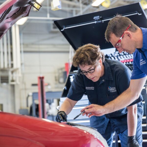 A student works with her professor on the engine of a red car at Austin Community College.