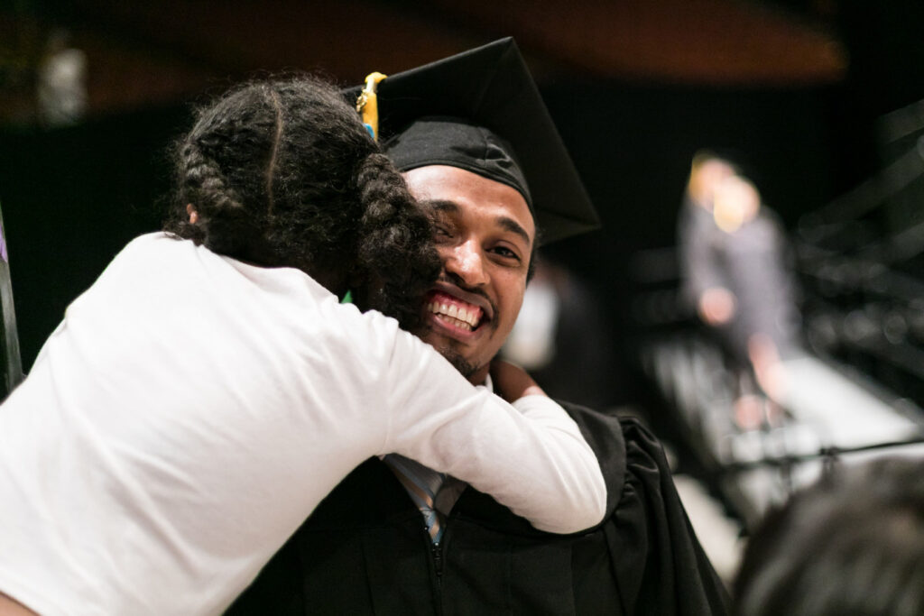 An ACC graduate is hugged by a family member during commencement ceremony. 