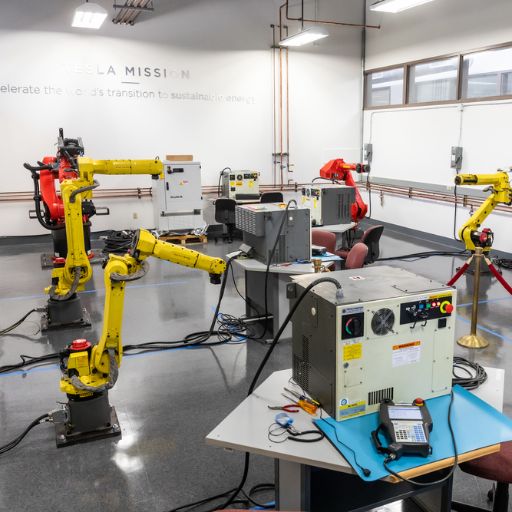 Yellow robot arms and red equipment stand ready in a manufacturing classroom.
