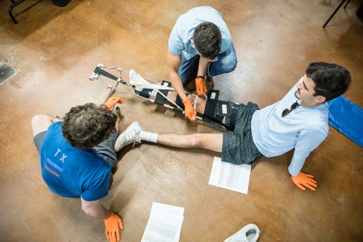 Two male ACC EMT students practice stabilizing a third student's leg in a a lab exercise in ACC's Emergency Medical Services Professions program