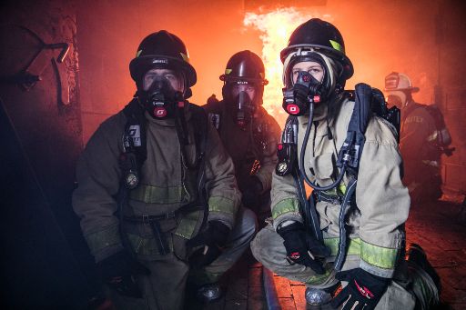 Three trainee firefighters in protective gear stand in front of blazing fire as part of their training in ACC's fire academy.