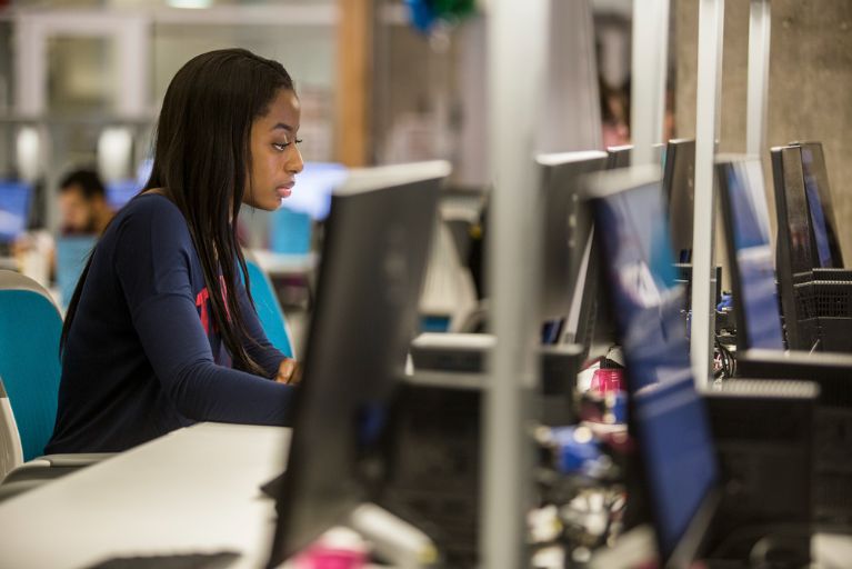 A Black student with long braids does schoolwork in the computer lab at ACC.