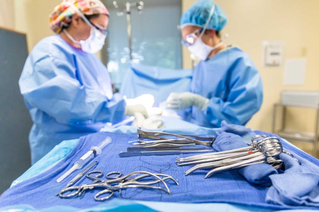 Students in hospital scrubs and masks at operating table in simulated surgical setting with tray of surgical instruments in the foreground