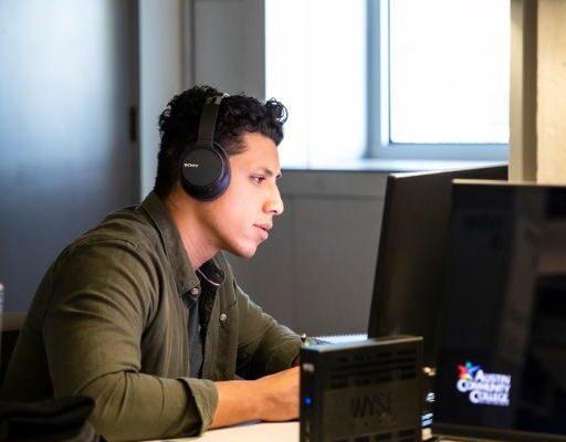 Student with dark hair, green shirt, and headphones studies at the computer.