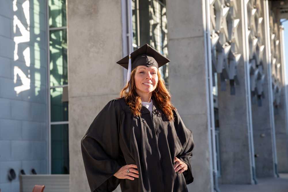 An ACC student poses in her graduation cap and gown in front of ACC Highland Campus building 1000.