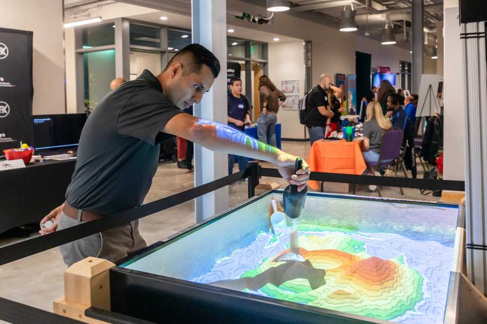 A young man experiments with the GIS department "TopoBox" which simulates topographic changes using computer technology and sand in a contained environment. 