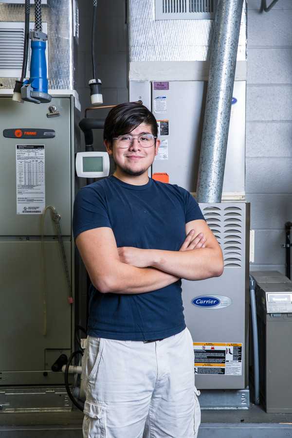 An ACC student poses in front of an HVAC system used for instructional purposes. 