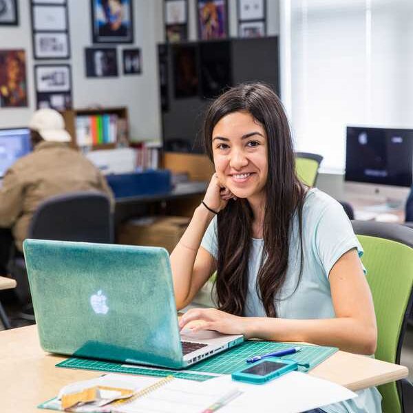 ACC student sitting at a desk infront of her laptop smiling at the camera.