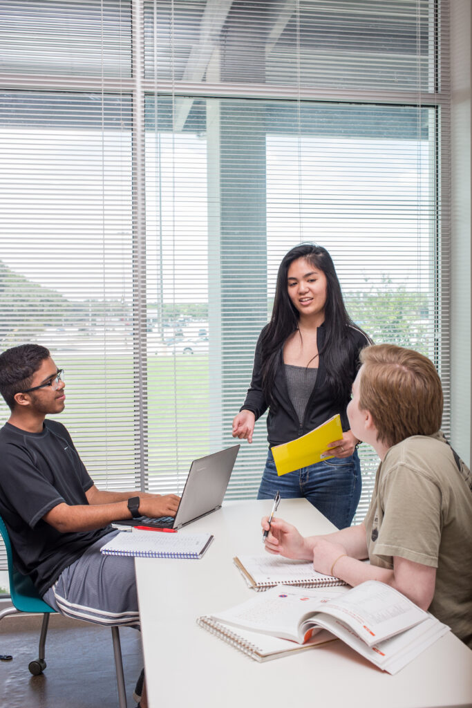 Three students worth togethe on a project with a laptop and notebooks in a classroom