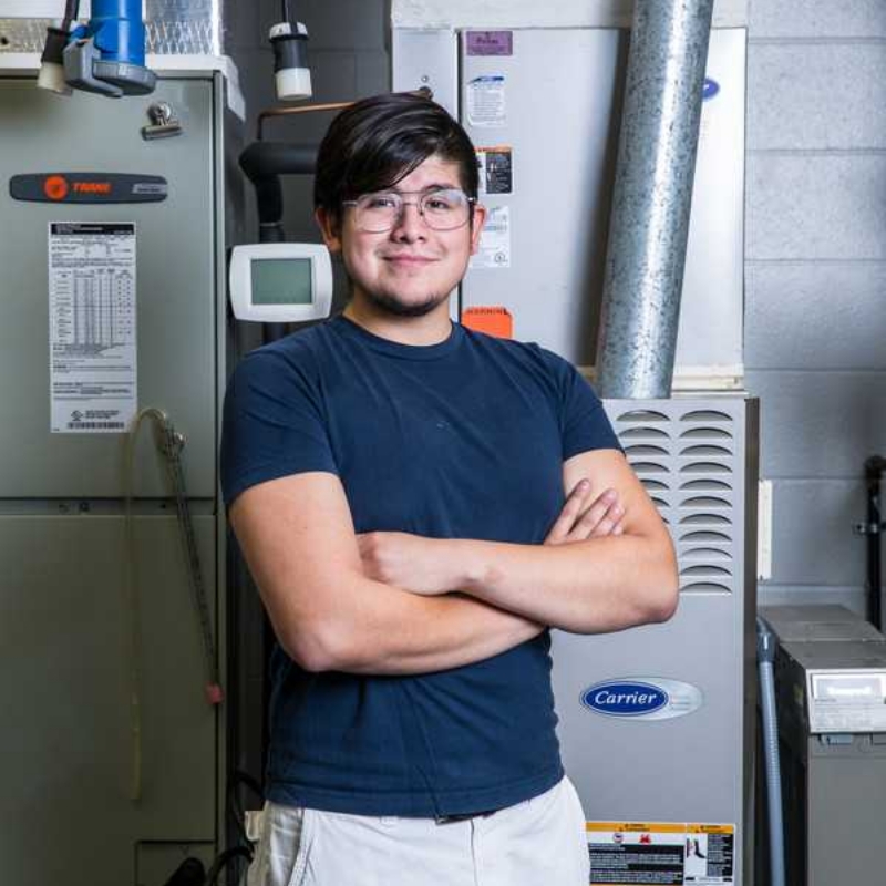 An ACC student poses in front of an HVAC system used for instructional purposes. 