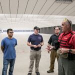 An ACC Public Safety Training Center instructor in a red safety vest instructs three criminal justice associate degree students on the shooting range.