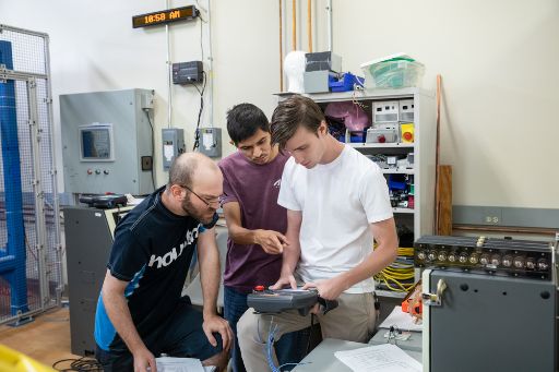 Three students in a robotics class work with a handheld controller in an advanced manufacturing class.