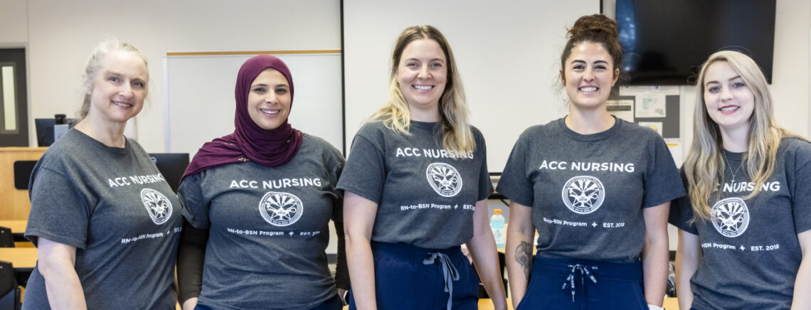 Five Rn-to_BSN students stand posing for a group photo wearing matching program t-shirts.