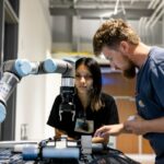 Two manufacturing students, one male and one female, program a robotic arm