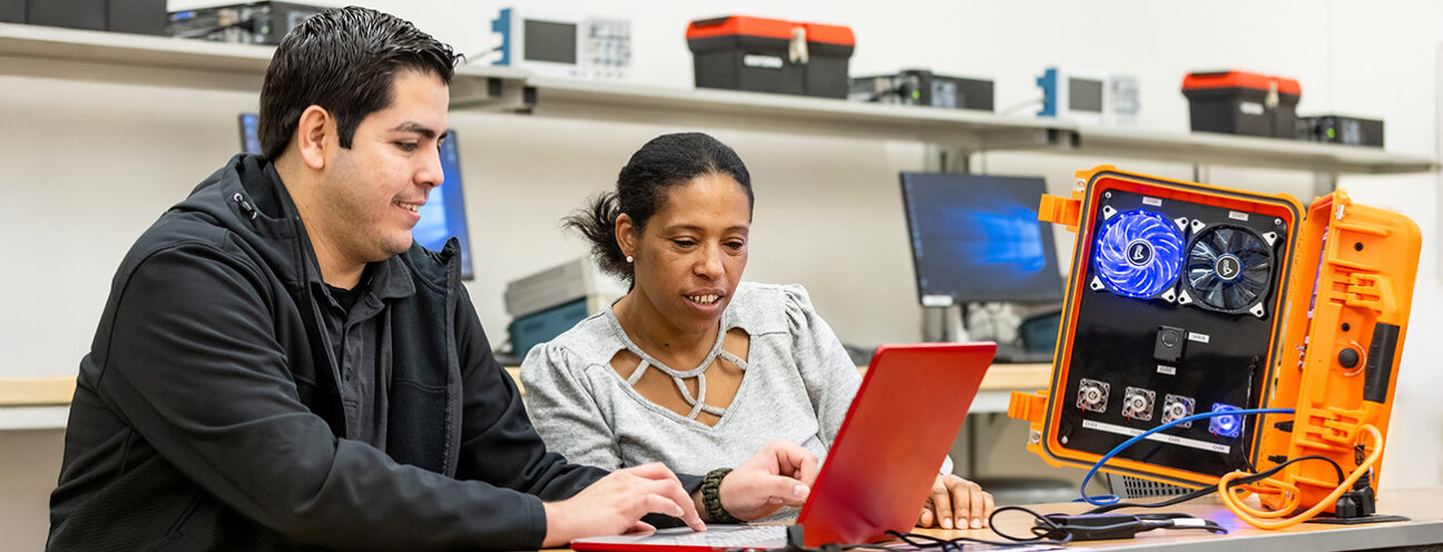 ACC students work on a laptop near other technical equipment
