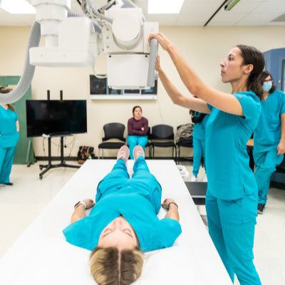 ACC Radiology students practice skills in their field. An ACC Radiology student in green scrubs is lying on a table, appearing relaxed and ready for a medical procedure.