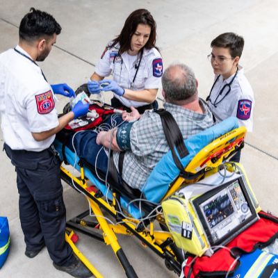 ACC EMT students assist a patient on a stretcher, providing care and support during a medical emergency simulation.