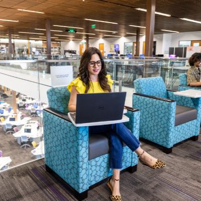 A female ACC student working on a laptop while sitting comfortably in a chair, surrounded by a warm and inviting atmosphere.