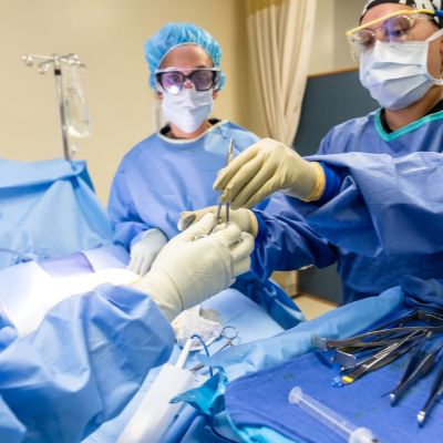 ACC Surgical Technology students in blue scrubs focused on performing a surgical procedure in an operating room.